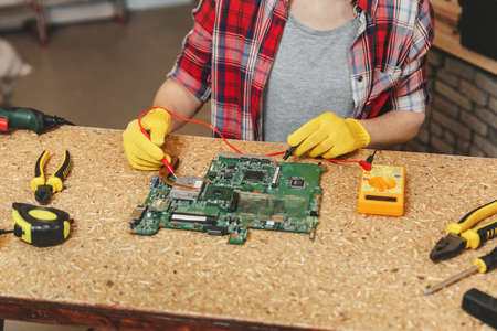 Multimeter for electrician. Close up of woman in yellow gloves, glasses digital electronic engineer...