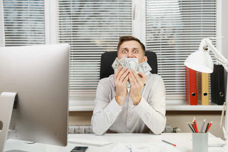 Happy smiling business man in shirt sitting at the desk with lot of cash money, working at computer...