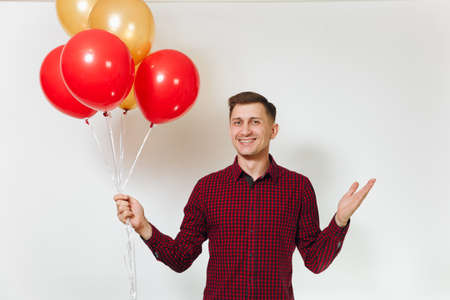 Handsome caucasian smiling fun young happy man 25-30 years in red plaid shirt with yellow golden balloons, celebrating birthday, on white background isolated for advertisement. Holiday, party conceptの写真素材