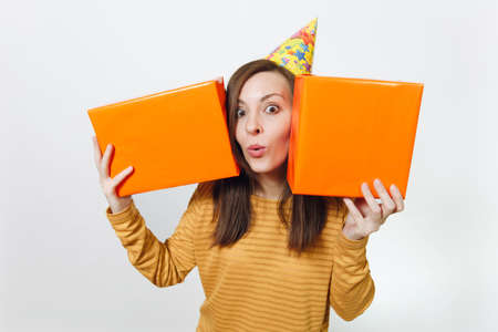 Beautiful caucasian fun young happy woman in yellow clothes, birthday party hat holding orange gift...