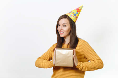 Cheerful young happy woman in yellow clothes, birthday party hat holding golden gift box with present, celebrating holiday on white background isolated for advertisement. With place for textの写真素材