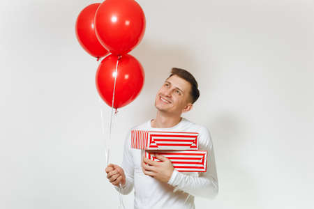 Handsome fun caucasian young happy man in longsleeve with red balloons, striped gift boxes with present, celebrating birthday, on white background isolated for advertisement. Holiday, party conceptの写真素材