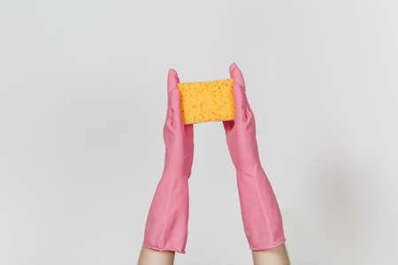 Close up of female hands in pink gloves horizontal holds yellow-orange sponge for cleaning and washing dishes isolated on white background. Cleaning supplies concept. Copy space for advertisement.の写真素材