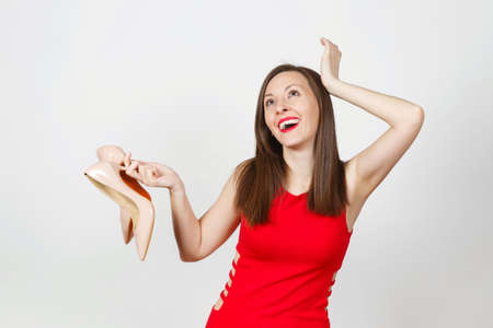 Attractive glamour happy caucasian fashionable young smiling brown-hair woman in red dress getting beige shoes with red sole of her shopping isolated on white background. Copy space for advertisementの写真素材