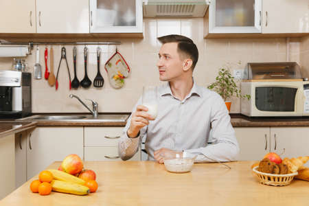 Handsome caucasian young business man in plaid shirt having breakfast, sitting at table, eating...
