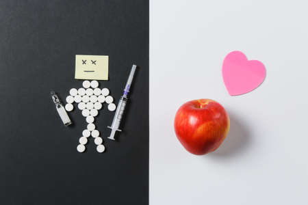 Medication round tablets arranged sad human on white black background. Apple, ampoule, empty syringe needle, heart, pills design. Treatment choice, healthy lifestyle concept. Copy space advertisementの写真素材