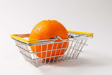 Close up of metal grocery basket for shopping in supermarket with lowered yellow handles with big bright orange isolated on white background. Concept of shopping. Copy space for advertisement.の写真素材