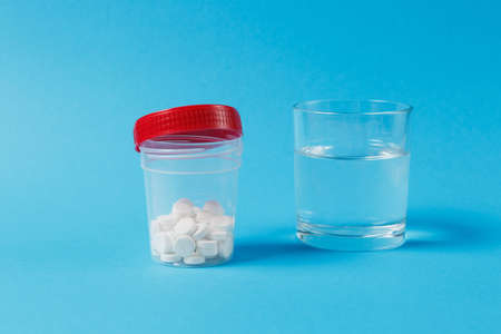 Medication jar with white round tablets arranged abstract on blue color background. Aspirin, glass water pills for design. Health treatment choice healthy lifestyle concept. Copy space advertisementの写真素材
