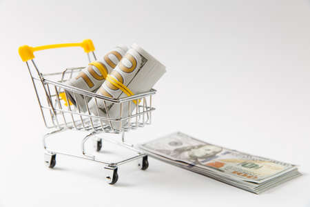 Supermarket grocery push cart for shopping with yellow elements on handle with bundles of dollars money banknote cash isolated on white background. Concept of shopping. Copy space for advertisementの写真素材