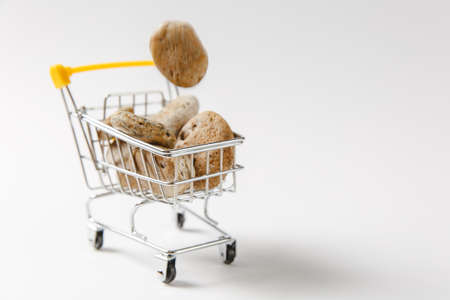 Close up of supermarket grocery push cart for shopping with yellow plastic elements on handle with stones falling in it isolated on white background. Concept of shopping. Copy space for advertisement.の写真素材