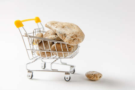 Close up of supermarket grocery push cart for shopping with yellow plastic elements on handle filled with brown stones isolated on white background. Concept of shopping. Copy space for advertisement.の写真素材