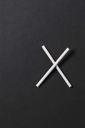 Two crossed white cigarettes like letter X on black background. Health, choice, healthy lifestyle concept. Copy space for advertisement. With place for text. Stop smokeの写真素材