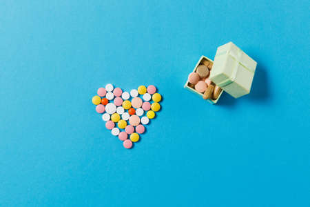 Medication white, colorful round tablets in form of heart isolated on blue background. Square shape box with lot pills. Concept of health, treatment, choice, healthy lifestyle. Copy space advertisingの写真素材