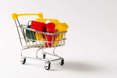Close up of supermarket grocery push cart for shopping with yellow handle filled with multi-colored geometric shapes isolated on white background. Concept of shopping. Copy space for advertisement.の写真素材