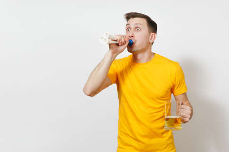 Inspired young fun cheerful European man, fan or player in yellow t-shirt hold pint mug of beer, football pipe cheer favorite team isolated on white background. Sport, student, play lifestyle conceptの写真素材