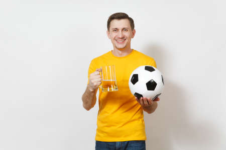 Inspired young smiling European man, fan or player in yellow uniform hold pint mug of beer, soccer ball cheer favorite football team isolated on white background. Sport, play, lifestyle conceptの写真素材
