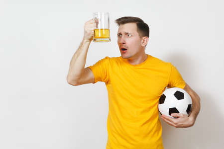 Inspired young fun bewildered European man, fan or player in yellow uniform hold pint mug of beer soccer ball cheer favorite football team isolated on white background. Sport, play, lifestyle conceptの写真素材
