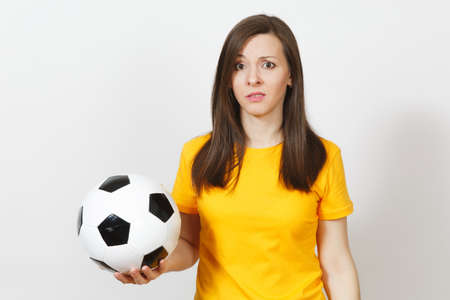 Pretty European young sad upset woman, football fan or player in yellow uniform holds soccer ball, worries about losing team isolated on white background. Sport, play football, lifestyle conceptの写真素材