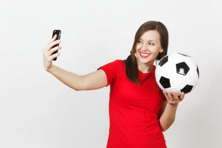 European young woman, fun pony tails, football fan or player in red uniform hold soccer ball, doing selfie on mobile phone isolated on white background. Sport play football, healthy lifestyle conceptの写真素材