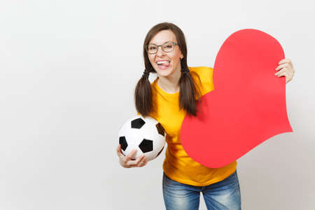 Smiling European woman, fun pony tails, football fan or player in glasses, yellow uniform hold classic soccer ball, red heart isolated on white background. Sport, football, healthy lifestyle conceptの写真素材