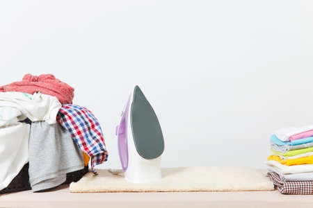 Close up steam iron, ironing colorful clothes, washed laundry, family clothing on ironing board isolated on white background. Housekeeping concept. Copy space for advertisement. With place for textの写真素材