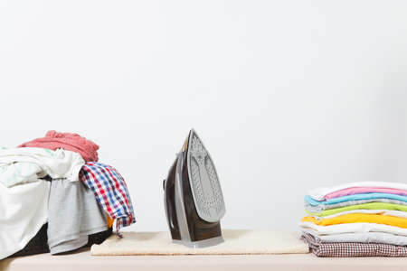 Close up steam iron, ironing colorful clothes, washed laundry, family clothing on ironing board isolated on white background. Housekeeping concept. Copy space for advertisement. With place for textの写真素材