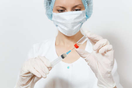 Doctor woman in face mask, sterile hat, gloves draws liquid medicine from bottle with syringe with...