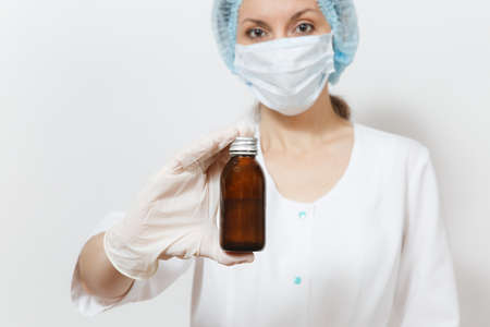 Doctor woman in face mask, sterile hat, gloves holding liquid medicine in bottle isolated on white background. Female doctor in medical gown. Healthcare personnel, health medicine concept. Copy spaceの写真素材