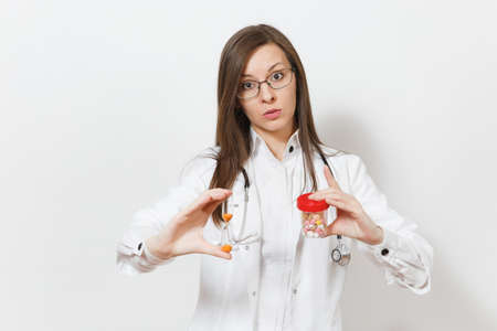 Upset doctor woman with stethoscope, glasses isolated on white background. Female doctor in medical gown holds hourglass, bottle with pills. Healthcare personnel medicine concept. Time is running outの写真素材