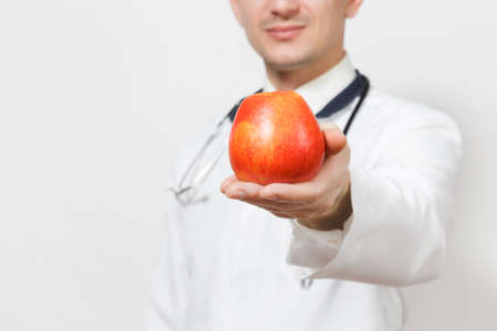 Close up cropped portrait doctor man isolated on white background. Male doctor in medical uniform, stethoscope holding red apple. Healthcare personnel, health concept. Proper nutrition. Copy spaceの写真素材