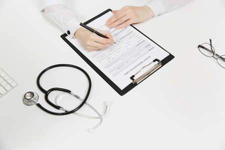 Doctor hands working filling out medical documents in light office in hospital. Woman writing on...