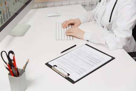 Close up woman sitting at desk, working with medical documents, clipboard with disease history in light office in hospital.の写真素材