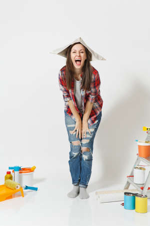 Full length portrait of woman in newspaper hat standing near instruments for renovation apartment home isolated on white background. Wallpaper, accessories for gluing, painting tools. Repair conceptの写真素材