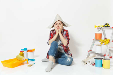 Shocked fun woman in newspaper hat sitting on floor with instruments for renovation apartment room isolated on white background.の写真素材