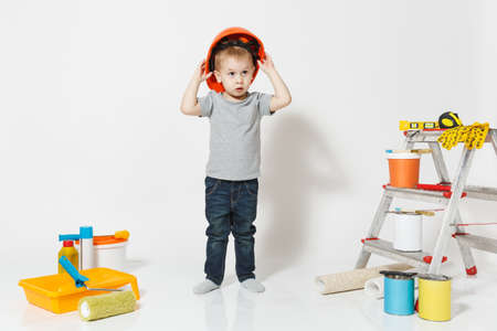 Little boy in orange protective helmet with instruments for renovation apartment isolated on white...