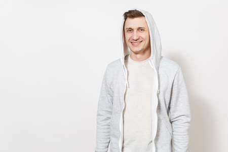Young handsome male student in t-shirt, blue jeans and light sweatshirt with hood rejoices and smiling in the studio on white background. Concept of emotions, good mood. Copy space for advertisementの写真素材