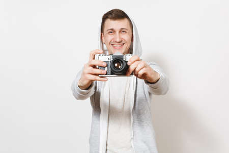 Young handsome excited student in t-shirt and light sweatshirt with hood with headphones holds retro camera in hands and shows it to camera in studio on white background. Concept of photography.の写真素材