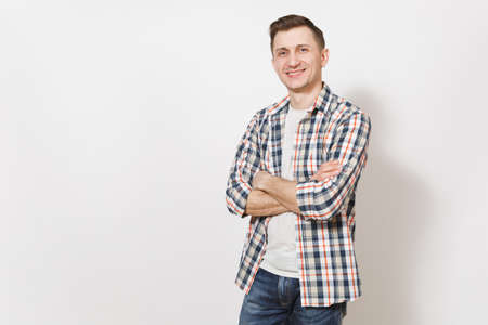 Young handsome happy smiling man in gray t-shirt, blue jeans, checkered shirt holding hands crossed over chest isolated on white background. Emotions concept, good mood. Copy space for advertisementの写真素材