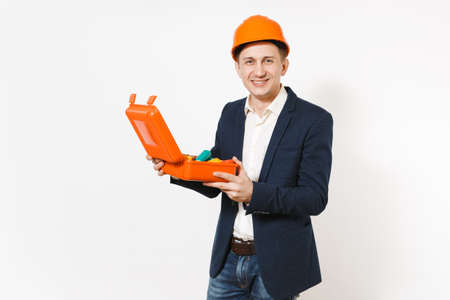 Young smiling businessman in dark suit, protective construction helmet holding opened case with...