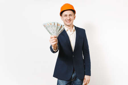 Smiling businessman in dark suit, protective hardhat holding bundle of dollars, cash money and pointing index finger up on copy space isolated on white background. Male worker for advertisementの写真素材