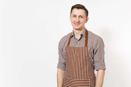 Young smiling calm man chef or waiter wearing striped brown apron, shirt posing isolated on white background. Male housekeeper or houseworker looking camera. Domestic worker for advertisementの写真素材
