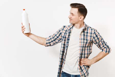 Young housekeeper man in checkered shirt holding white empty cleaning bottle with cleaner liquid isolated on white background. Male and house chores. Copy space advertisement. Cleanliness conceptの写真素材