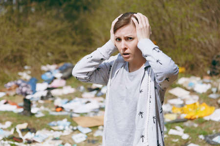 Close up Young shocked woman in casual clothes cleaning clinging to head near pile of rubbish in...