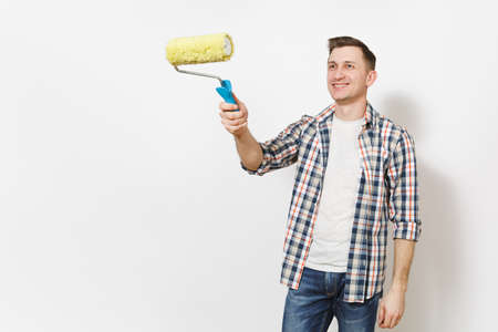 Young smiling handsome man in casual clothes pointing paint roller for wall painting on copy space isolated on white background. Instruments, tools for renovation apartment room. Repair home conceptの写真素材
