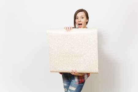 Young shocked beautiful woman in casual clothes holding unrolled wallpaper roll isolated on white...
