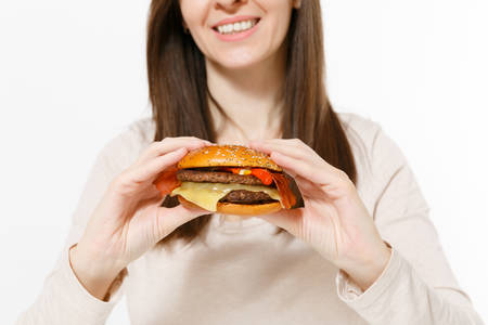 Close up cropped shot smiling woman in light clothes holds in hands burger isolated on white background. Proper nutrition or American classic fast food. Copy space for advertisement. Advertising areaの写真素材
