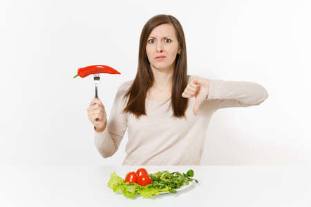 Sad woman at table with leaves salad lettuce, tomatos on plate, pepper on fork isolated on white background. Proper nutrition, vegetarian food, healthy lifestyle dieting concept. Area to copy spaceの写真素材