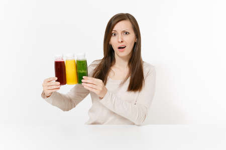 Young woman at table with green, red and yellow detox smoothies in bottles isolated on white background. Proper nutrition, vegetarian drink, healthy lifestyle, dieting concept. Area to copy spaceの写真素材