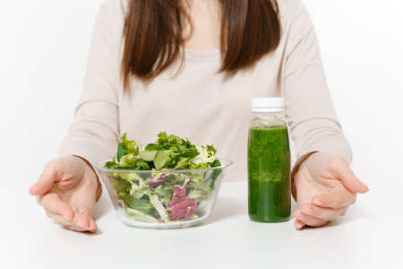 Close up cropped woman at table with green detox smoothies, salad in glass bowl isolated on white...