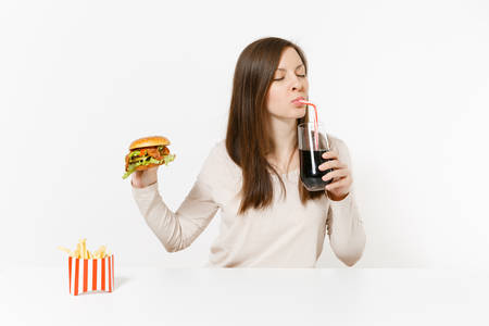 Woman drink cola from straw glass bottle, sitting at table with burger, french fries isolated on...